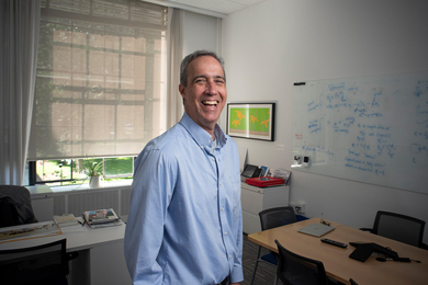 Dan Huttenlocher standing in an office, wearing a button-down shirt and laughing