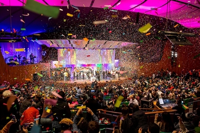 Photo of Kresge Auditorium showing confetti in the air, students on stage, and a full house audience cheering on the celebration.