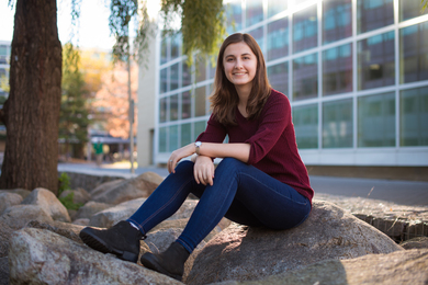 Eliza Wells sits on the large boulders in between the Alumni Pool and Building 56.