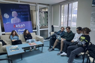 Six students sitting around in a lounge. Four of them are looking at a laptop screen.