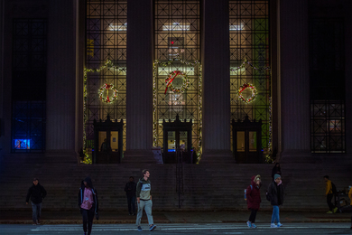 The steps and front entrance of MIT at 77 Massachusetts Avenue is pictured. There are wreaths and string lights above each of the three doors.