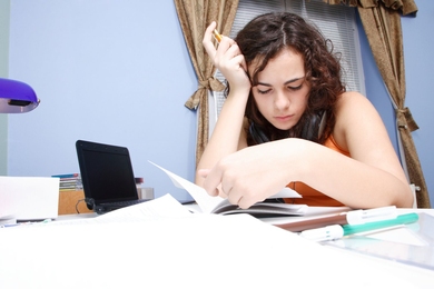 A woman sitting at a cluttered desk, reading a book