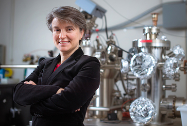  MIT Professor Bilge Yildiz stands with arms folded in her MIT lab with large metallic equipment behind her