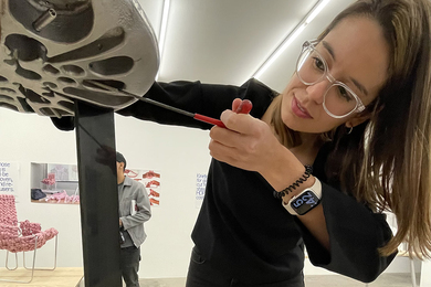 Highly distorted photo of Maria Risueño Dominguez adjusting a screw on a round silver plate attached to a black metal furniture leg 