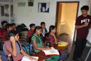 Photo of Siddhartha Jayanti in a small classroom teaching Indian children as they take notes, with the white background shaded in the colored dot style of a comic book