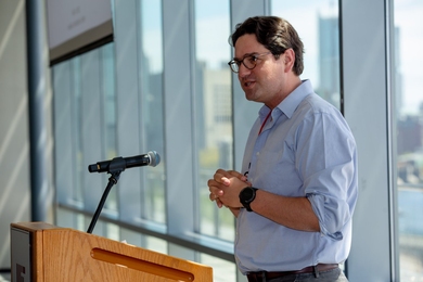 Photo of Giovanni Traverso speaking at a podium before a wall of glass windows