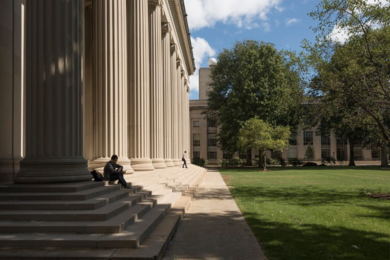 Photo of MIT's Building 10 and Killian Court in summer, focusing on columns and steps (at left) and verdant trees and grass (at right)