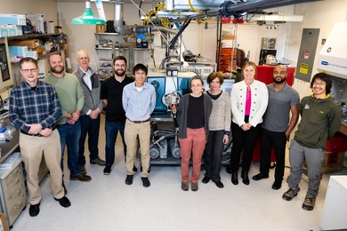 Group photo of 10 Lincoln Laboratory staff members posing in front of heavy equipment in a lab