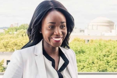 Ezinne Uzo-Okoro is pictured outside, smiling and gazing off to the right. Green trees and the MIT dome are in the background
