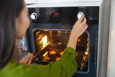 Photo in which the viewer looks over the shoulder of a young woman as she adjusts a dial on her oven, setting it to 350 degrees