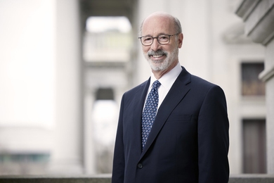 Tom Wolf poses in front of an out-of-focus building