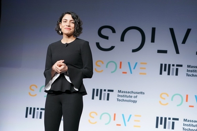 Hala Hanna stands on a well-lit stage in front of a backdrop that reads, "MIT Solve" and "Massachusetts Institute of Technology"