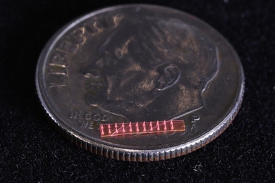 Image of a red microneedle array on a U.S. dime. The array is a small fraction of the area of the coin.