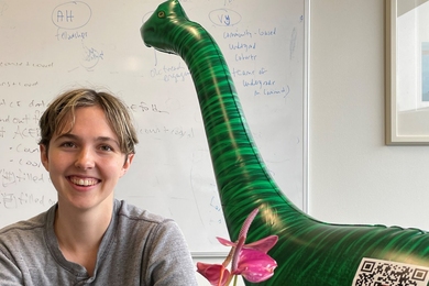 Kelsey Merrill sits in an office with the Vote-a-Saurus inflatable dinosaur in the background.