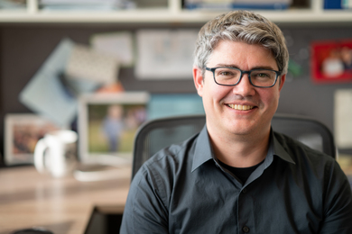 McDonald smiles while sitting at his desk, with blurry office background.