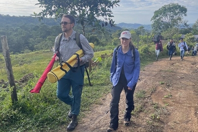 Sean Anklam and Marcela Angel lead a larger group down a dirt road in a verdant, mountainous area of Colombia