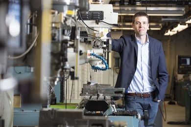 John Hart stands next to 3D printing hardware in a laboratory
