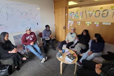 Seven people sit around a small table, talking
