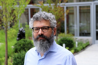 Portrait photo of Keeril Makan standing in a courtyard with lush greenery and a wall of windows in the background.