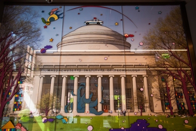 Image taken from Killian Court with Building 10 and the MIT dome centered in the background. Overlaid on the photograph are whimsical illustrations such as the MIT Hack of a police car on the dome.