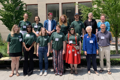 Two rows of 14 library staff members pose in a group in an outdoor courtyard.