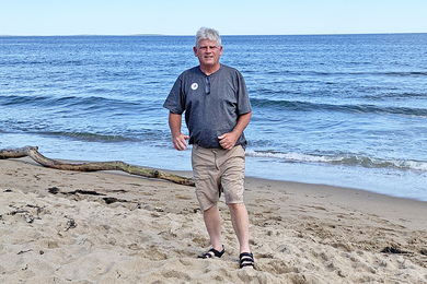 Photo of Steven Goldman standing on a beach with clear water and clear skies behind him