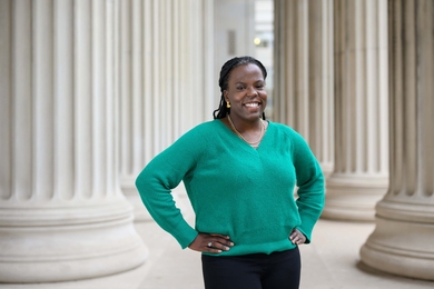 Asia Allison stands with hands on hips, smiling, amidst columns on MIT's campus