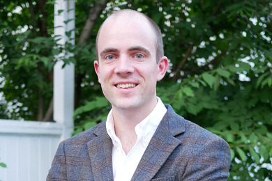 Headshot of Richard Fletcher outdoors, with green foliage behind him