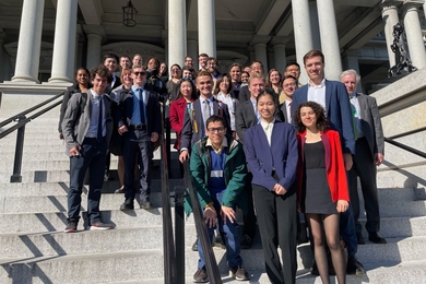 About 30 people, including 26 MIT students, pose on the steps of the Eisenhower Executive Office Building.