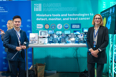 Jeremy Li and Ana Jaklenec stand in front of a demonstration booth, with half a dozen microscopes showing screens of biological samples. A banner behind them reads: "Cancer Nanomedicine: Miniature tools and technologies to detect, monitor, and treat cancer"
