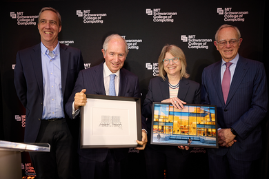 Dan Huttenlocher, Stephen Schwarzman, Sally Kornbluth, and L. Rafael Reif stand against a backdrop featuring the MIT Schwarzman College of Computing logo. Kornbluth holds a framed photo of a glass building, while Schwarzman holds a framed pencil drawing of the same building.