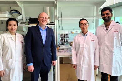 A woman and three men flank the microbioreactor system, which is about the size of a small printer