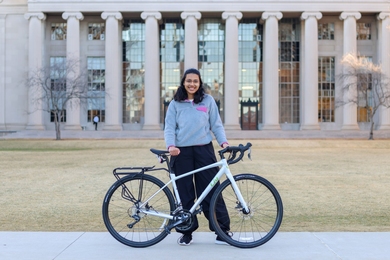 Amulya Aluru poses with her bicycle in front of the columns of MIT's Building 10