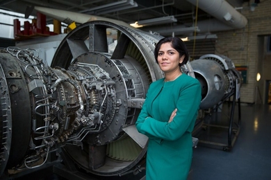 Hamsa Balakrishnan stands in a lab next to an engine that's taller than she is