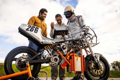 3 students gather around an orange motorcycle with a partially exposed design, showcasing intricate mechanical components