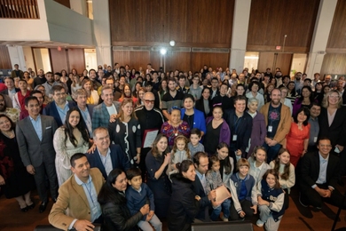 Hundreds of people stand or kneel in a large hall