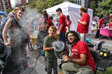 Scientists in red T-shirts demonstrate an air cannon to a child