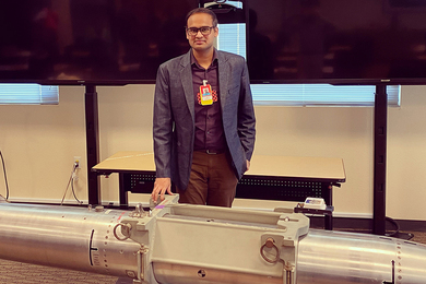 Kunal Singh stands before a silver missile in a room with a flat screen behind him