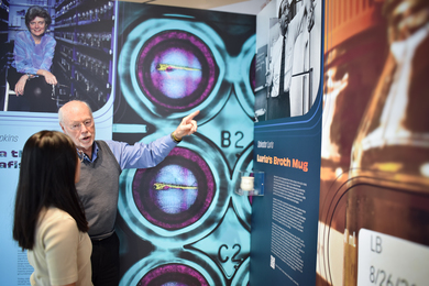 Phillip Sharp and an unidentified woman chat in front of panels of a gallery exhibit