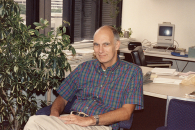 Hale Bradt poses while seated at his desk, with a large potted plant at left