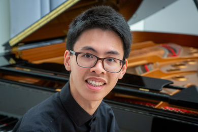 Holden Mui poses for a photo before an open grand piano