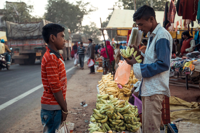 A young boy and young vendor chat over bananas in a market in Padhar, India.