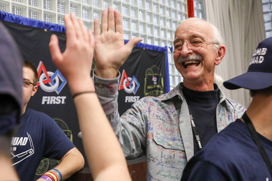 Woodie Flowers high-fives FIRST Robotics competitors wearing blue tshirts