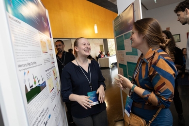 Two people wearing lanyards talking in front of a poster