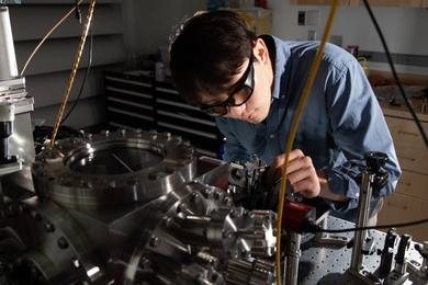 A man wearing safety goggles leans over a machine in an MIT lab