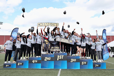 About 20 MIT women's team members and three coaches celebrate on the podium by throwing their hats in the air 