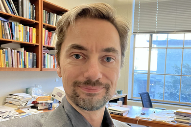 Headshot of Laurent Demanet with bookshelf and window behind him