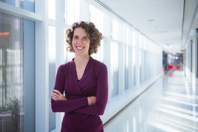 Darcy McRose standing with her arms folded in a daylit hallway with windows