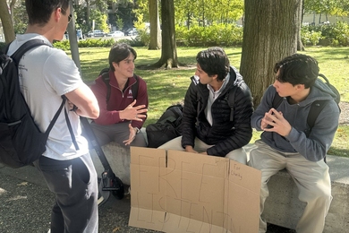 Four students sitting outside with a crude cardboard sign that reads "Free Listening for charity"