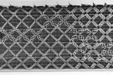 A black and white image of a woven metamaterial, comprised mostly of diamond-shaped cells woven from spiral fibers